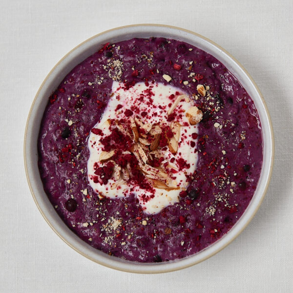 Low Carb Porridge in weißer Bowl mit Joghurt-Topping, Mandelblättchen, Chiasamen und gefriergetrockneten Himbeeren – Draufsicht