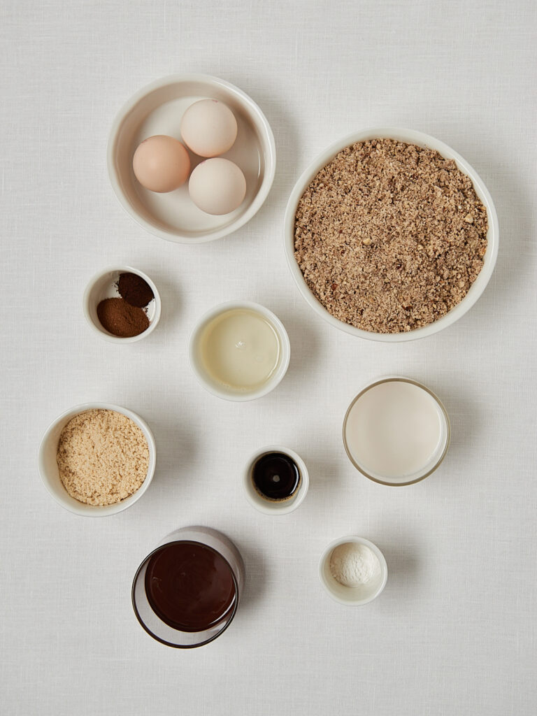 Flatlay Zutaten Low Carb Nusskuchen: Eier, gemahlene Haselnüsse, Schokolade, Vanille und weitere Zutaten in kleinen Schälchen