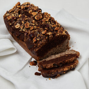 Ganzer Low Carb Nusskuchen mit gehackten Haselnüssen auf weißem Leinentuch, angeschnitten