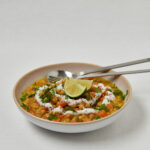 Linsensuppe mit Kokosjoghurt, Avocado und Limette in flacher Schale – seitliche Aufnahme