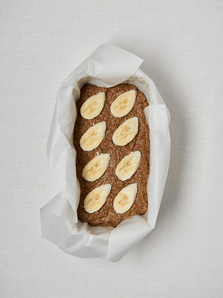 Roher Bananenbrot-Teig in Kastenform mit Bananenscheiben als Garnitur – Draufsicht