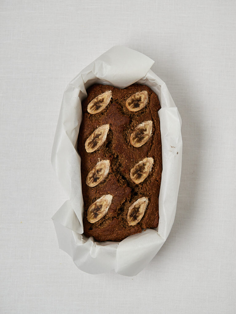 Protein Banana Bread in Backpapier-Kastenform mit Bananenscheiben vor dem Backen