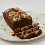 Ganzer Protein Banana Bread Laib mit Bananenscheiben-Garnitur auf weißem Teller