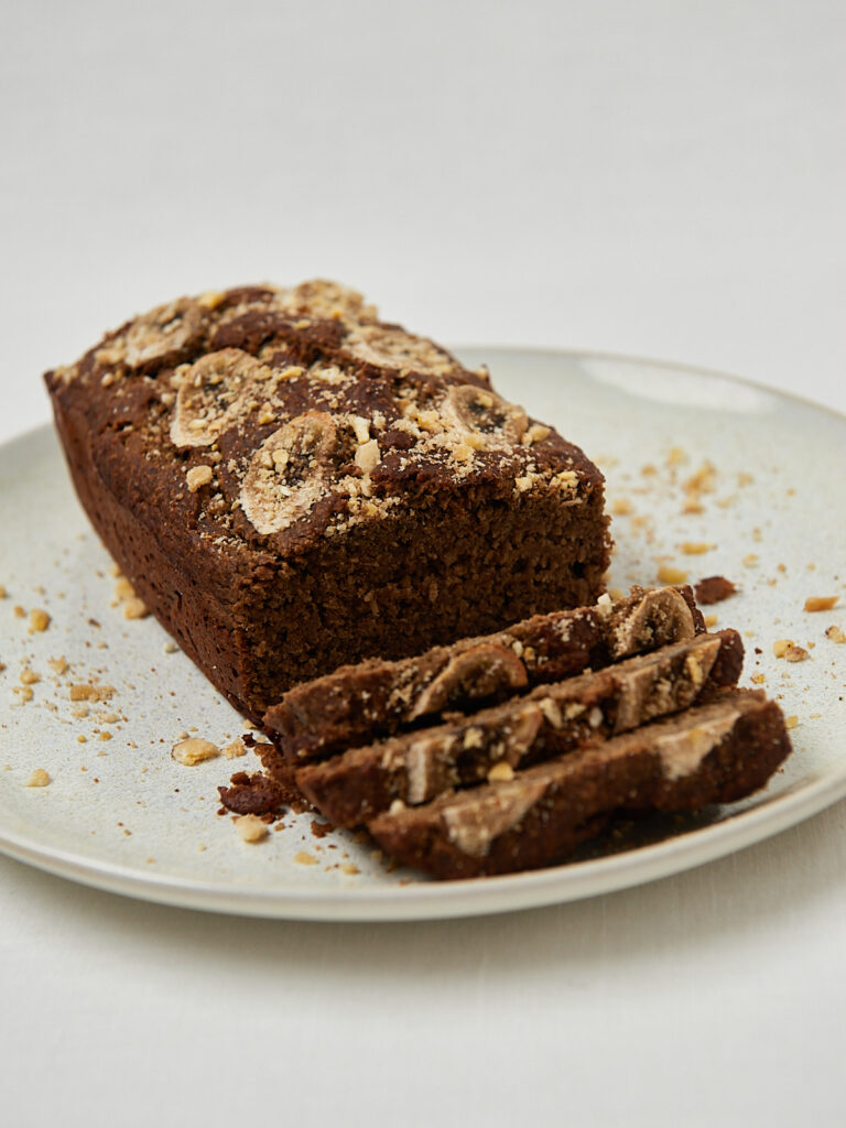 Ganzer Protein Banana Bread Laib mit Bananenscheiben-Garnitur auf weißem Teller