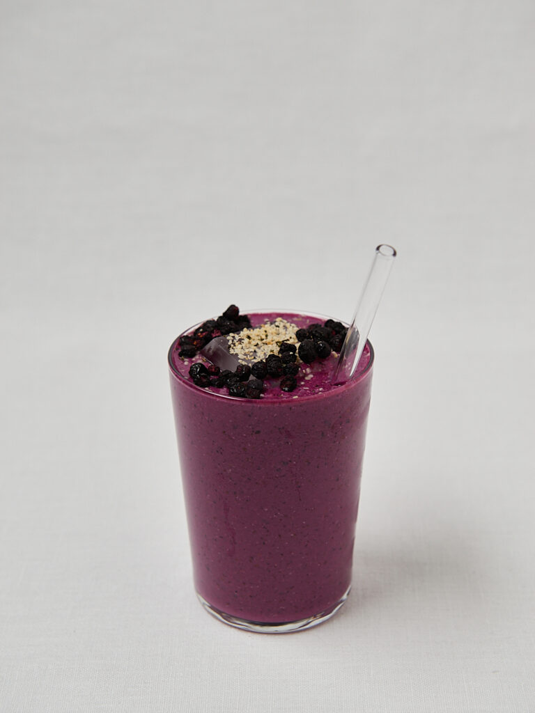 Super Power Shake im hohen Glas mit Hanfsamen und Beeren-Topping &ndash; seitliche Ansicht auf wei&szlig;em Hintergrund