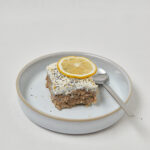 Zitronen Mohn Baked Oats mit Sojaquark-Topping und Zitronenscheibe auf blauem Teller – gesundes Frühstück