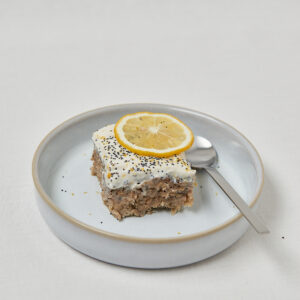 Zitronen Mohn Baked Oats mit Sojaquark-Topping und Zitronenscheibe auf blauem Teller – gesundes Frühstück