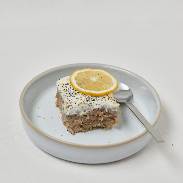 Zitronen Mohn Baked Oats mit Sojaquark-Topping und Zitronenscheibe auf blauem Teller – gesundes Frühstück