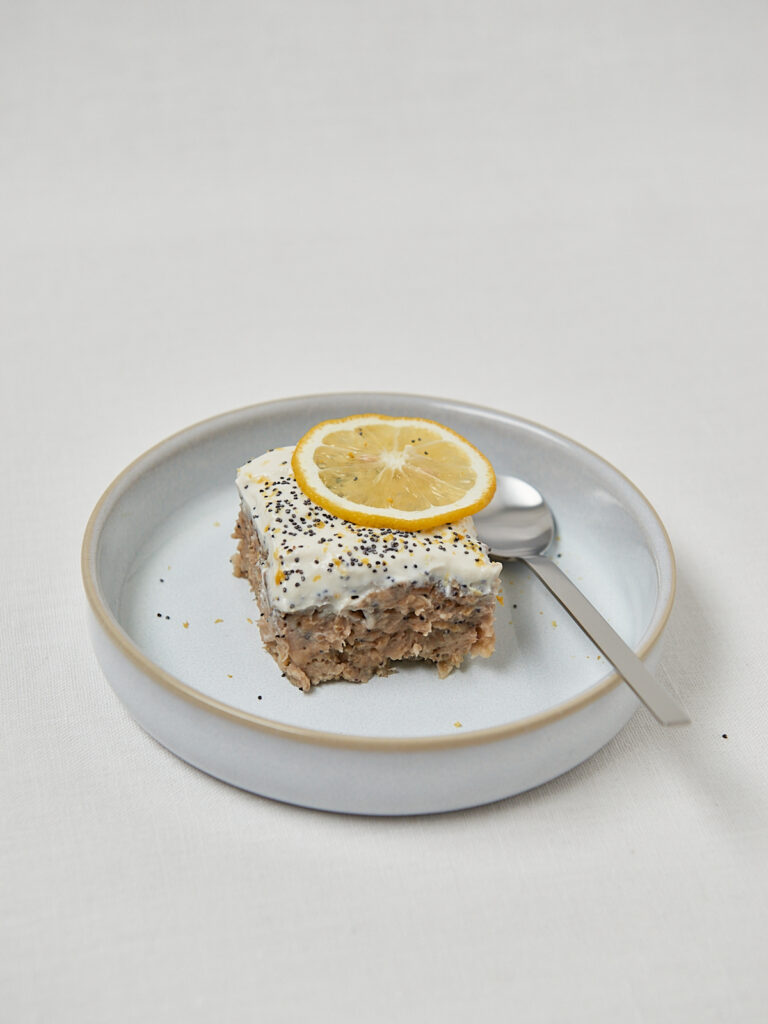 Zitronen Mohn Baked Oats mit Sojaquark-Topping und Zitronenscheibe auf blauem Teller – gesundes Frühstück