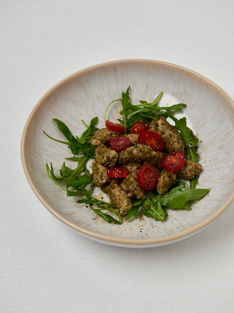 Gesunde Gnocchi mit Kirschtomaten und Rucola auf rundem Teller – seitliche Aufnahme