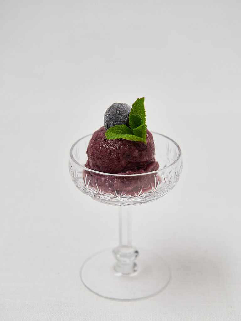 Blaubeer Frozen Dessert in Glasschale mit Minze &ndash; seitliche Aufnahme auf hellem Hintergrund