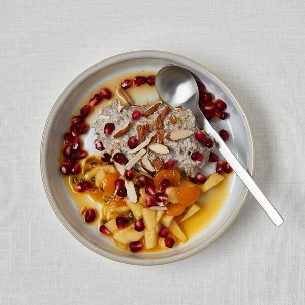 Overnight Oats mit Mango, Granatapfelkernen und Mandeln auf weißem Teller – Meal Prep