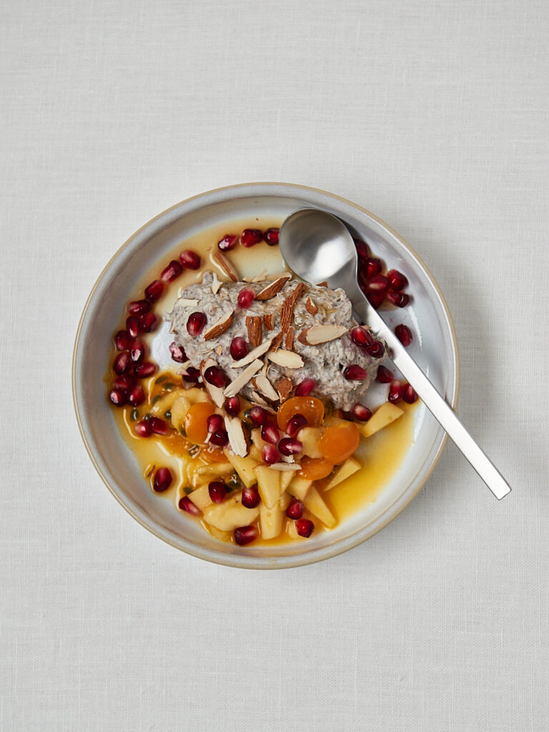 Overnight Oats mit Mango, Granatapfelkernen und Mandeln auf wei&szlig;em Teller &ndash; Meal Prep