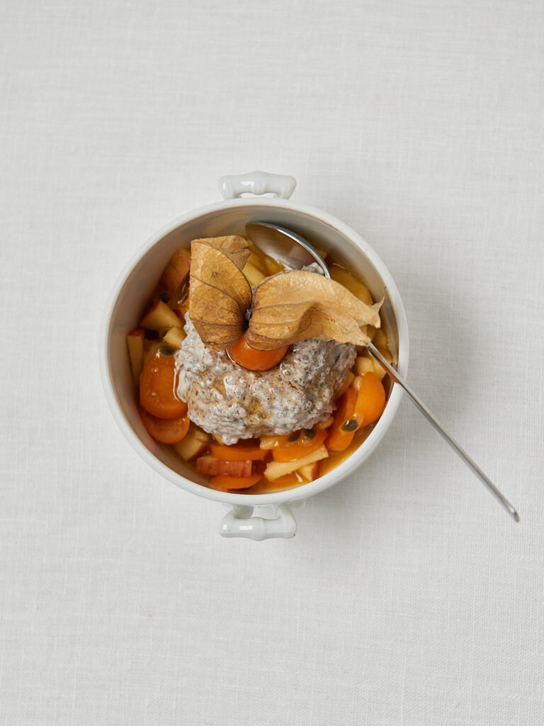 Bircher M&uuml;sli mit Mango, Granatapfel und N&uuml;ssen in wei&szlig;er Sch&uuml;ssel &ndash; Overhead Shot
