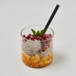 Chia Pudding mit Mango, Granatapfelkernen und Minze im Glas mit schwarzem Löffel – gesundes Meal Prep Frühstück