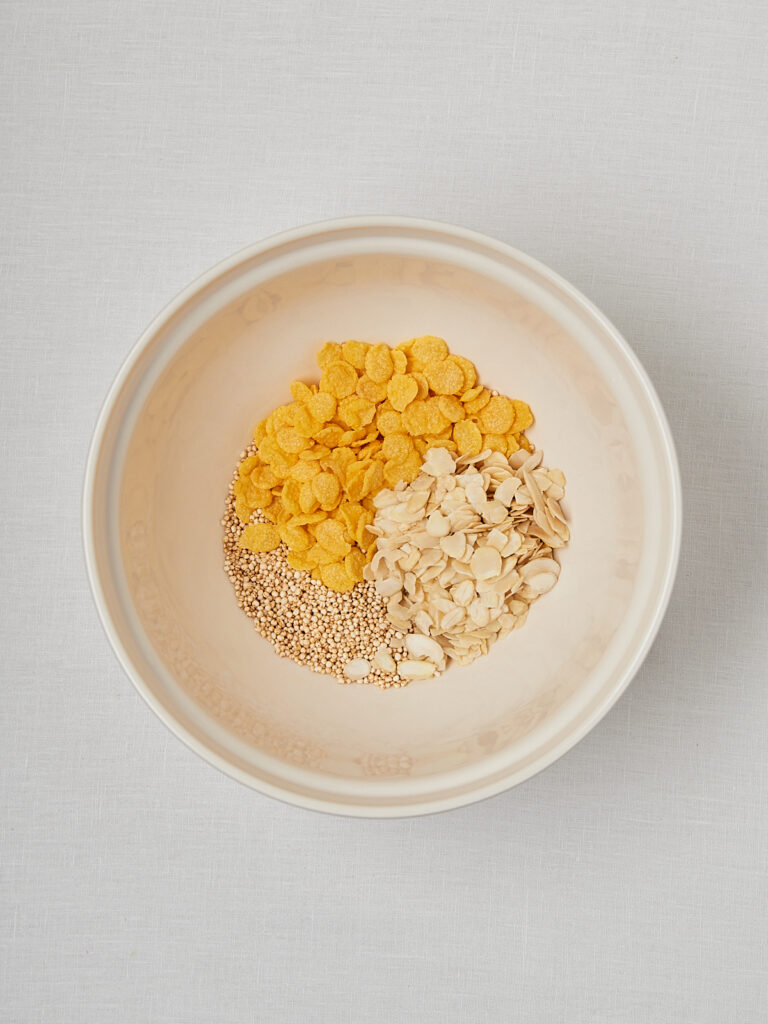 Cornflakes und Mandelbl&auml;ttchen in beiger Sch&uuml;ssel &ndash; Zutaten f&uuml;r Schokocrossies