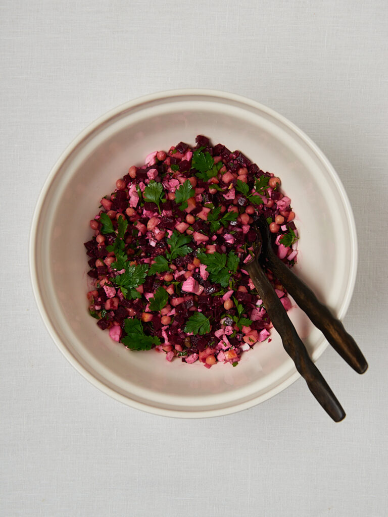 Rote Beete Salat mit Kichererbsen beim Vermengen mit schwarzer Zange &ndash; Zubereitungsschritt