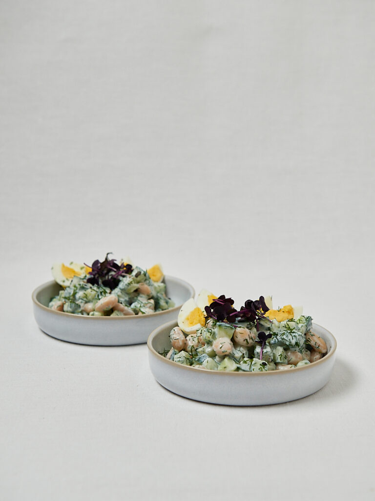Frische Gurken Joghurt Bowl mit weißen Bohnen und halbierten Eiern in zwei Schüsseln – gesundes Sommerrezept
