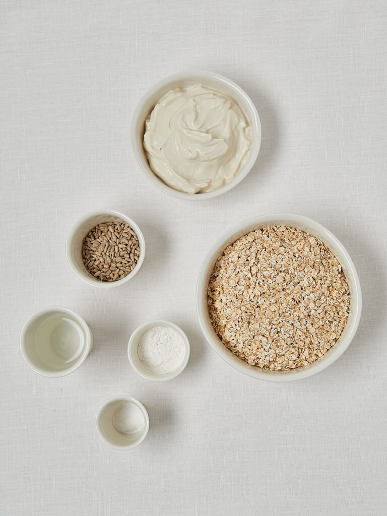 Zutaten-Flatlay Fitnesstangen &ndash; Joghurt, Sesam, Haferflocken und Gew&uuml;rze in Sch&auml;lchen