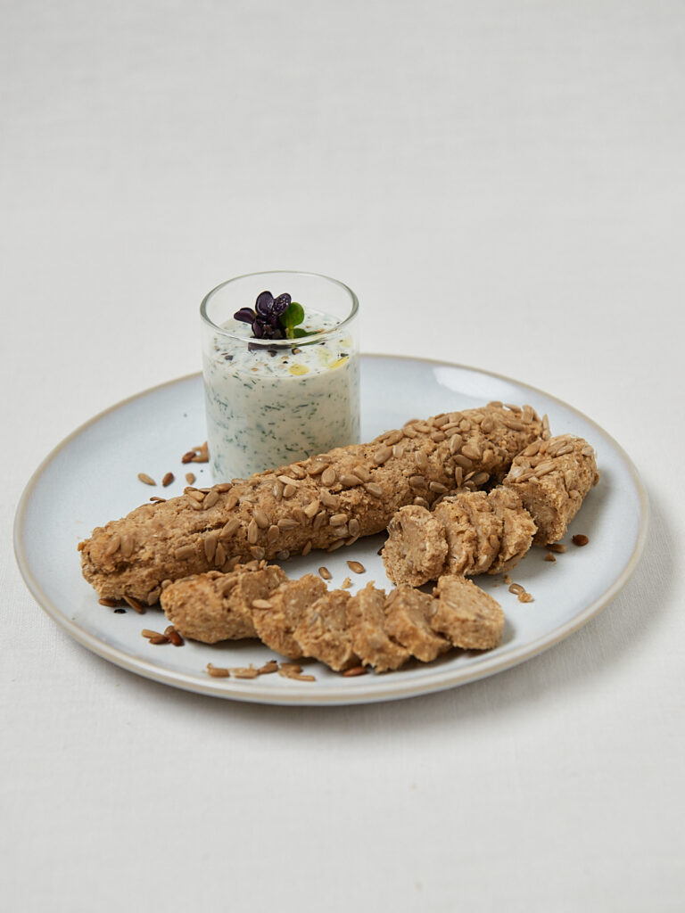 Fitnesstangen mit Sesam und Joghurt Dip in kleinem Glas auf wei&szlig;em Teller &ndash; gesunder Snack
