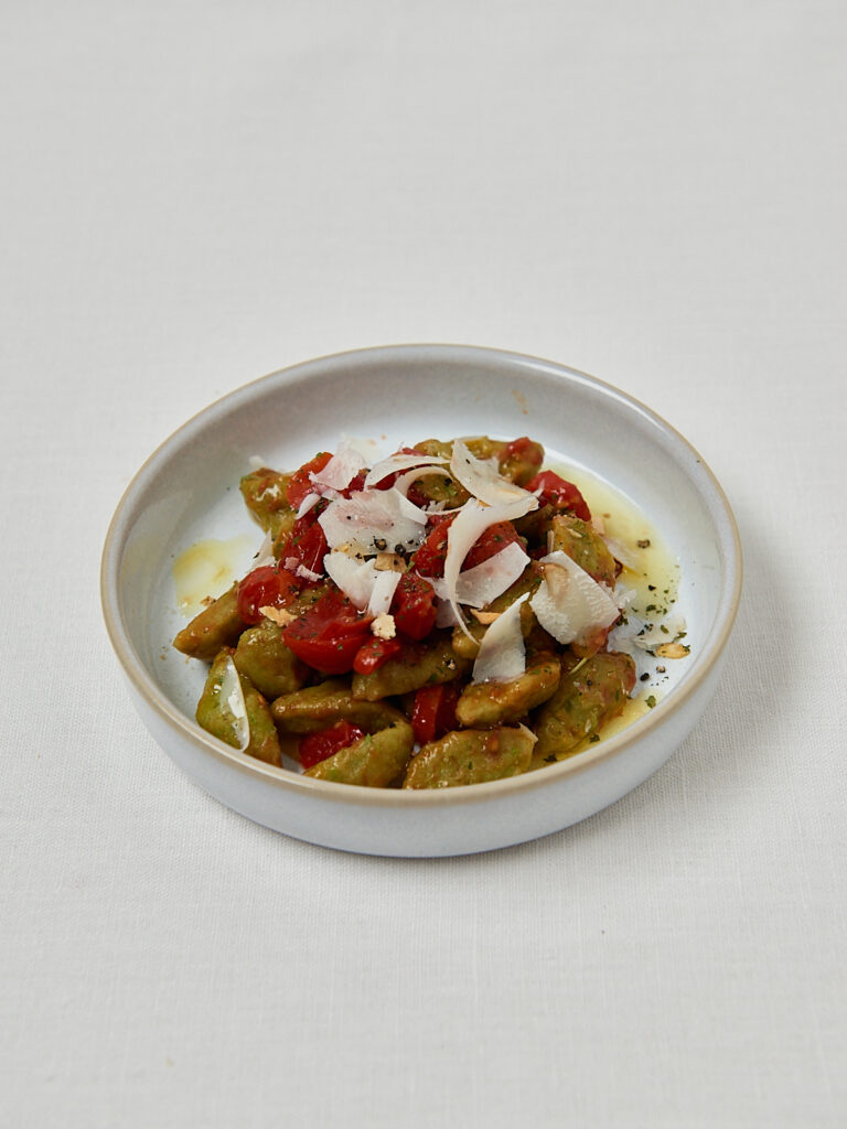 Gr&uuml;ne Erbsennudeln mit Kirschtomaten und Mozzarella auf rundem Teller &ndash; seitliche Aufnahme