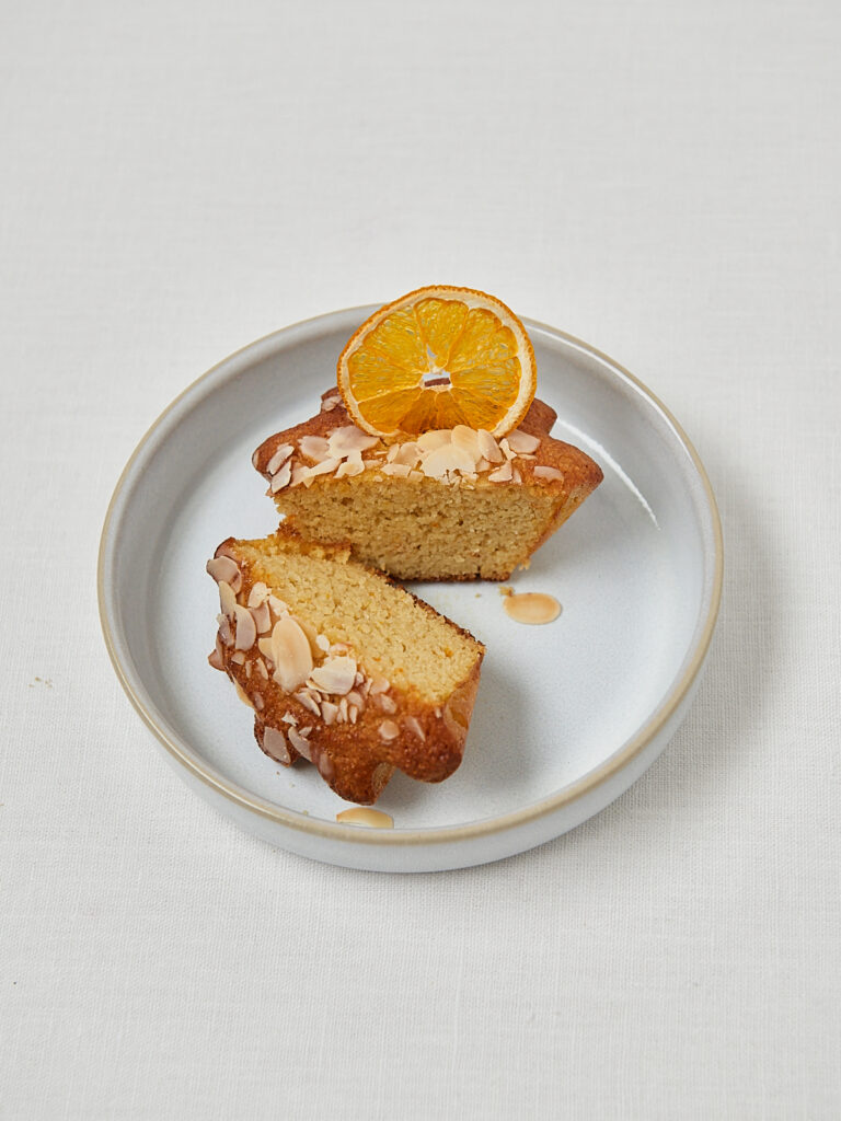 Glutenfreier Orangen Mandelkuchen mit Mandelbl&auml;ttchen auf rundem Teller &ndash; Studioaufnahme