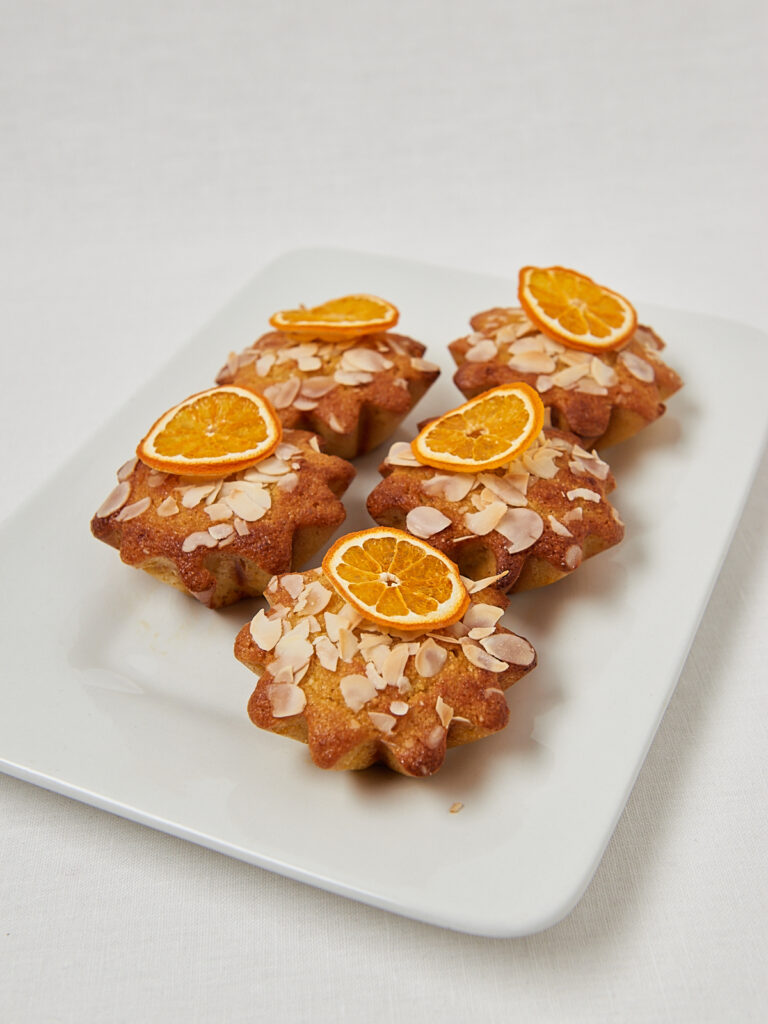Glutenfreie Orangen Mandel Muffins mit getrockneten Orangenscheiben auf eckigem Teller &ndash; Draufsicht