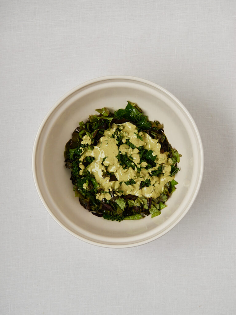 Gr&uuml;nkohl mit Pistazien und Dressing in beiger Sch&uuml;ssel &ndash; Zubereitungsschritt Overhead