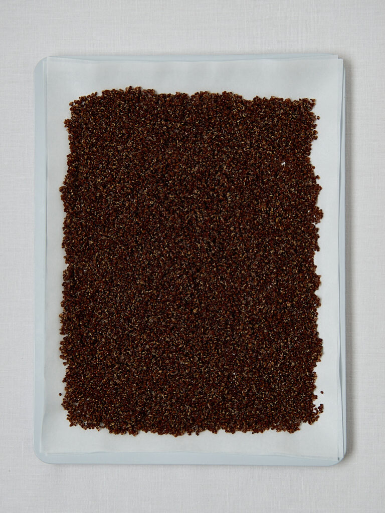 Crispy Quinoa auf wei&szlig;em Backblech vor dem Backen &ndash; Overhead Shot Zubereitungsschritt
