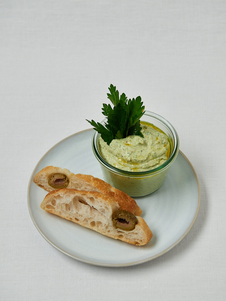 Green Olive Feta Dip in Glasschüssel mit frischer Petersilie – Draufsicht Studioaufnahme