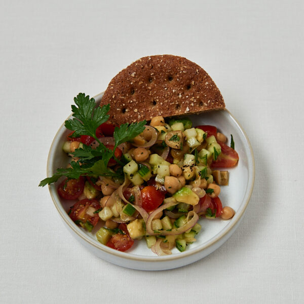 Gurken-Kichererbsen-Salat mit Granatapfelkernen und frischer Petersilie in weißer Schüssel mit Vollkorncracker