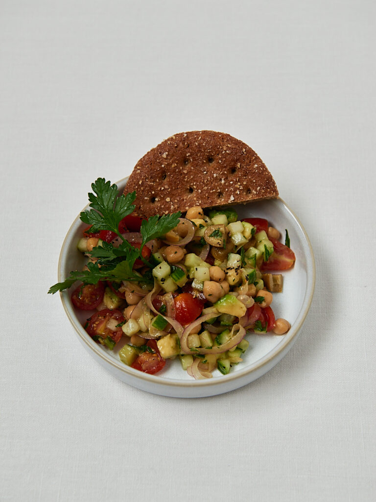 Gurken-Kichererbsen-Salat mit Granatapfelkernen und frischer Petersilie in wei&szlig;er Sch&uuml;ssel mit Vollkorncracker