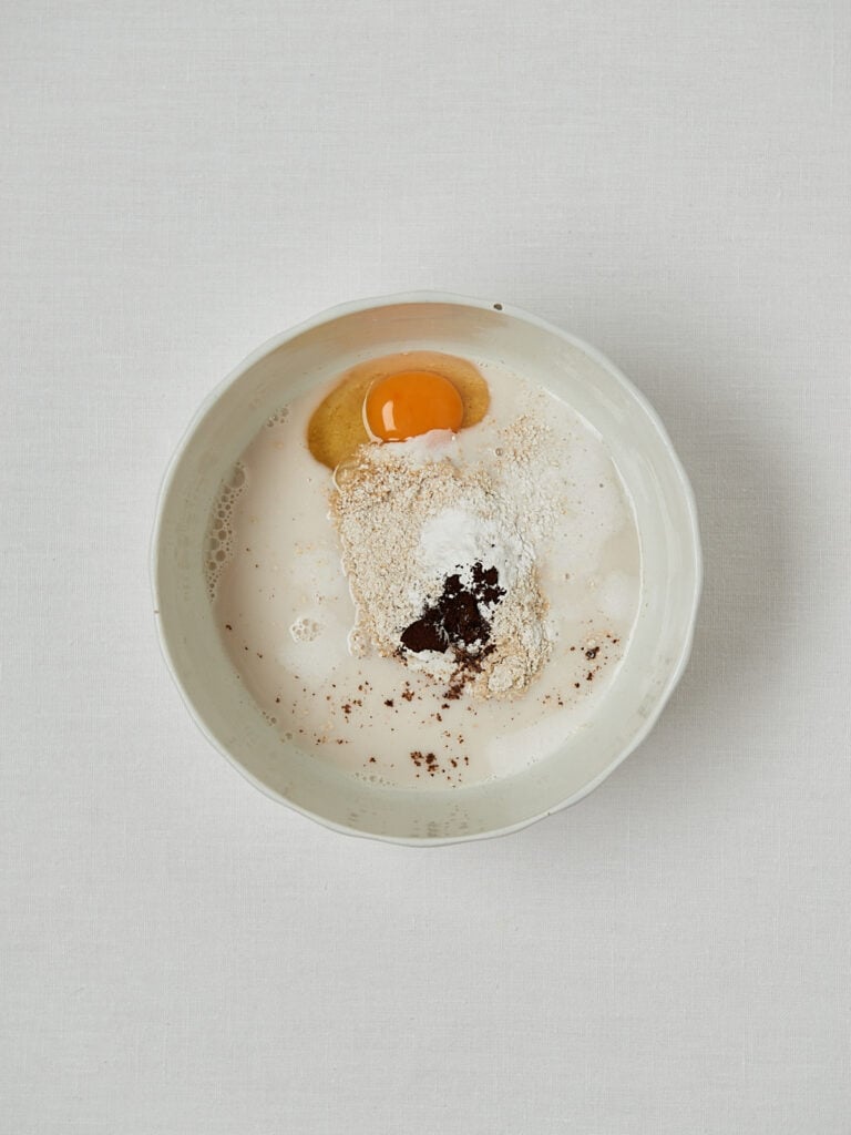 Zutaten-Flatlay Oatmeal Pancakes – Ei, Haferflockenmehl und Vanille auf hellem Untergrund