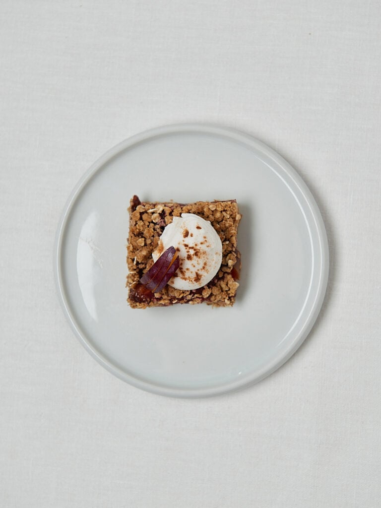 Crumble Riegel mit Pflaumenf&uuml;llung und Sahne auf wei&szlig;em Teller &ndash; Overhead Shot
