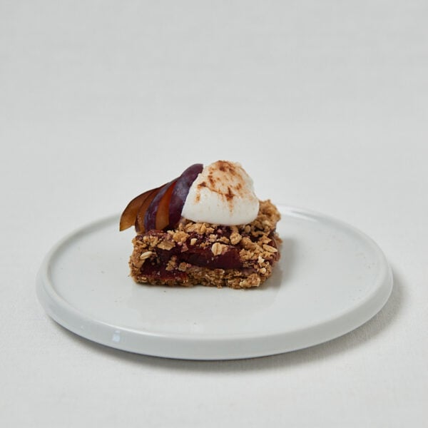 Pflaumen Crumble Bar mit Joghurt-Topping auf rundem Teller – seitliche Aufnahme