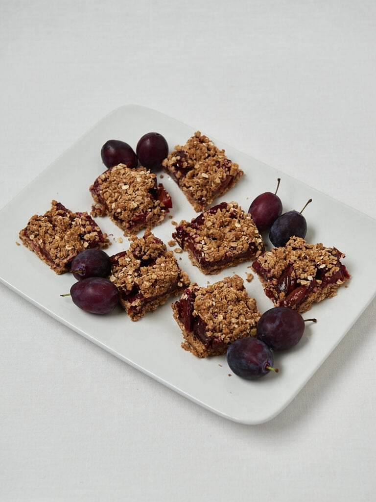 Crumble Bars mit Pflaumen und Beeren auf hellem Teller &ndash; Draufsicht Overhead Shot